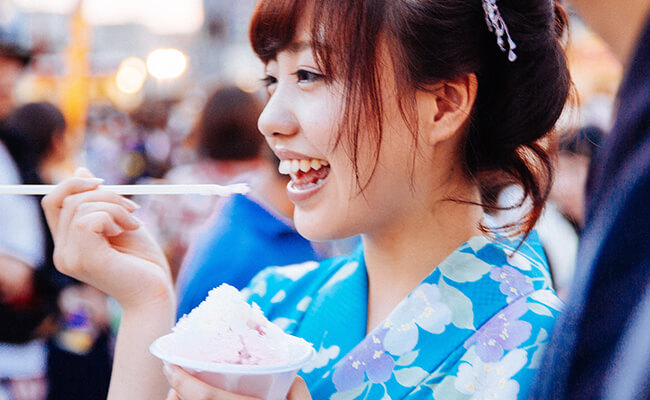 屋台でかき氷を美味しそうに食べる浴衣女子